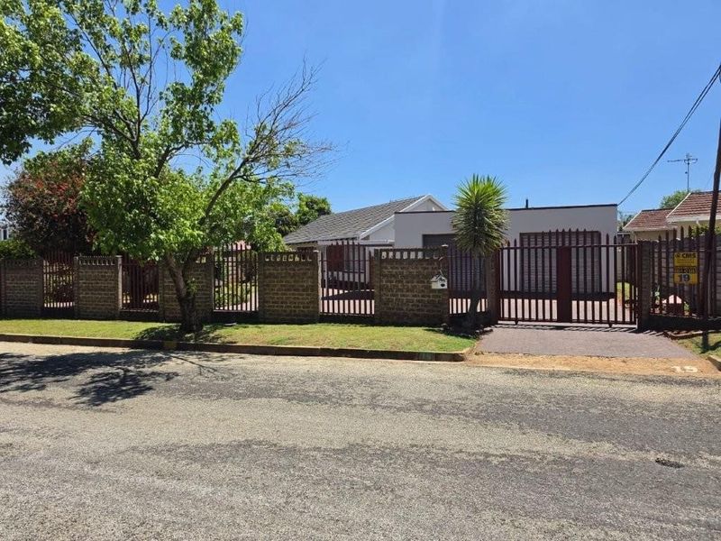 Front view of the property featuring a secure brick boundary wall, metal driveway gate, and paved entrance area.