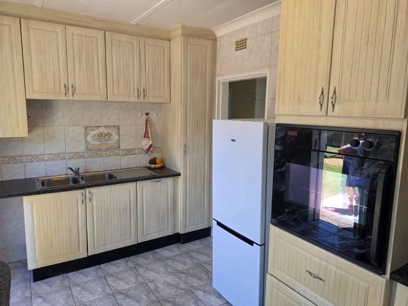 A functional kitchen featuring light-toned built-in cabinetry, a double sink, tiled backsplash, and a built-in oven with tiled flooring throughout.