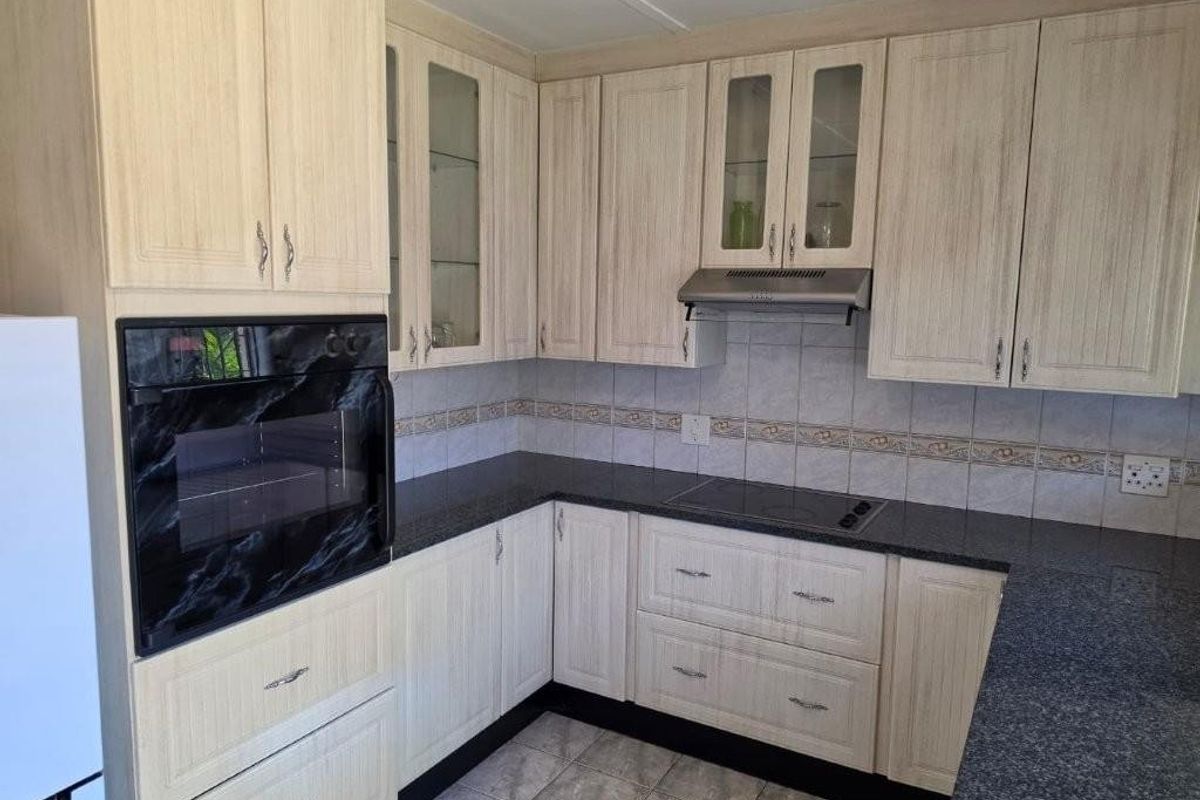A functional kitchen featuring light wood-grain cabinetry, dark granite countertops, built-in oven, electric cooktop, and a tiled backsplash.