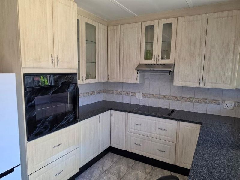 A functional kitchen featuring light wood-grain cabinetry, dark granite countertops, built-in oven, electric cooktop, and a tiled backsplash.