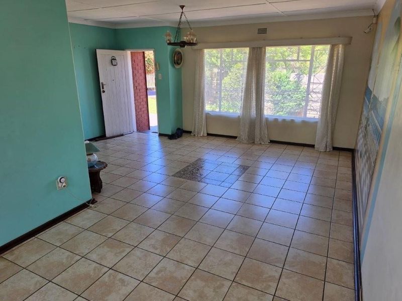 A spacious, empty living room featuring ceramic tile flooring, large windows providing natural light, and direct access to the exterior.