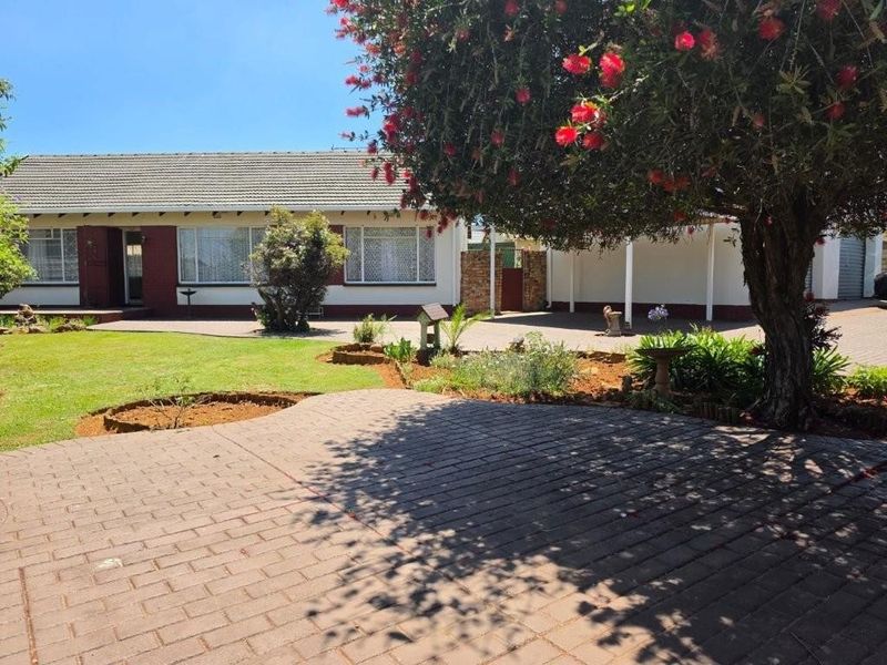 Front view of a single-story house featuring a paved driveway, well-maintained garden, and secure entrance area.