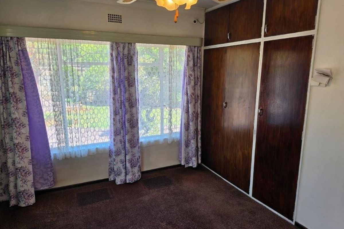 A bedroom featuring built-in wooden cupboards, a ceiling fan, and large windows overlooking the garden.