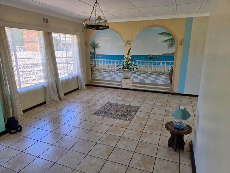 Spacious living area featuring large windows, tiled flooring, and a decorative wall mural, offering a blank canvas for modern interior design updates.