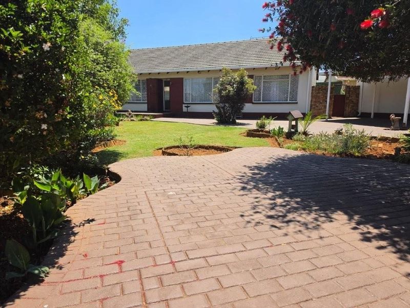 A well-maintained front exterior featuring a paved driveway, landscaped garden, and a classic brick facade with a tiled roof.