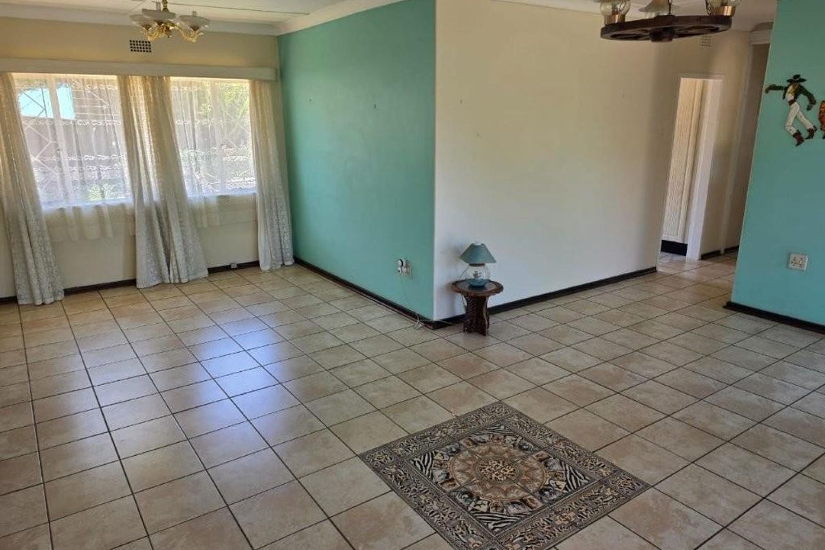 Spacious living area featuring tiled flooring with a decorative inlay, neutral and teal wall finishes, and ceiling lighting fixtures.