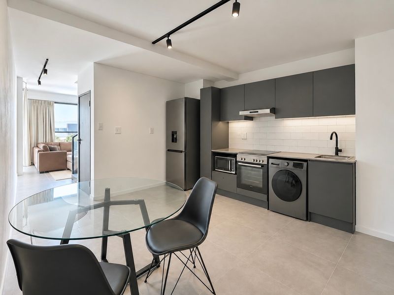 Modern open-plan kitchen featuring sleek dark cabinetry, subway tile backsplash, integrated appliances, and contemporary track lighting, seamlessly flowing into the living area.