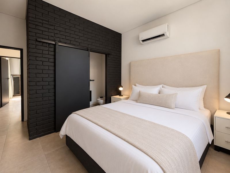 Modern bedroom featuring a striking black exposed brick feature wall, sliding barn door to en-suite, and split system air conditioning.