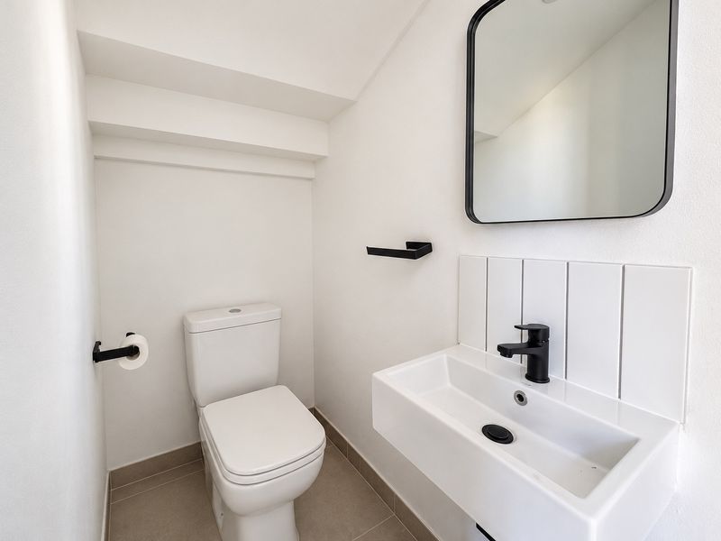 A modern, minimalist bathroom featuring a wall-mounted basin with black fixtures, a matching toilet, and a clean tiled splashback.