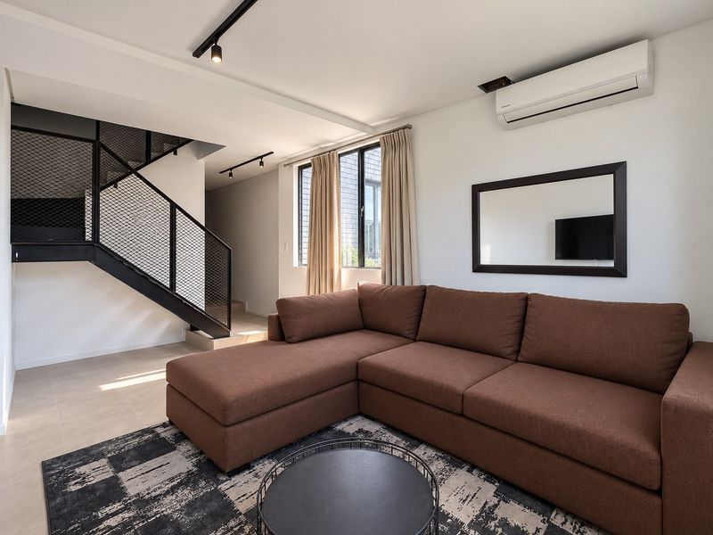 Modern living room featuring tiled flooring, track lighting, a split-system air conditioner, and a distinctive metal staircase with mesh balustrade.