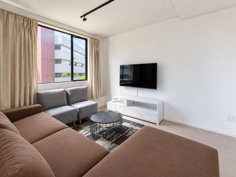 A bright and modern living room featuring tiled flooring, track lighting, and a large window providing natural light.