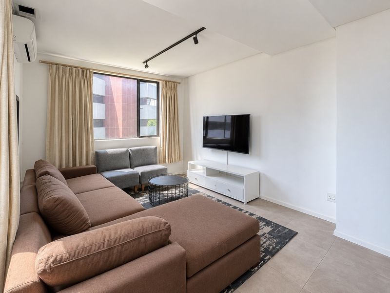 A bright and modern living room featuring tiled flooring, track lighting, and a wall-mounted air conditioning unit.