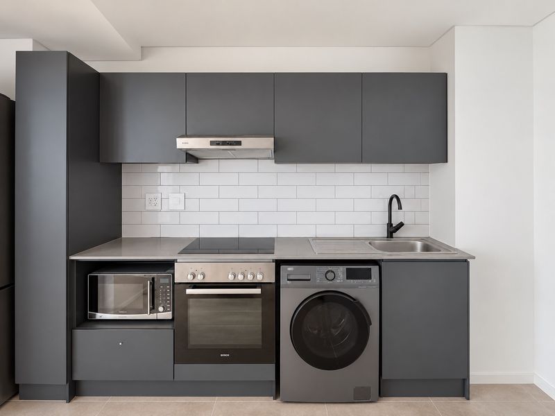 Modern kitchen featuring charcoal cabinetry, subway tile backsplash, integrated appliances including an oven, hob, extractor, microwave, and washing machine with a stainless steel sink.