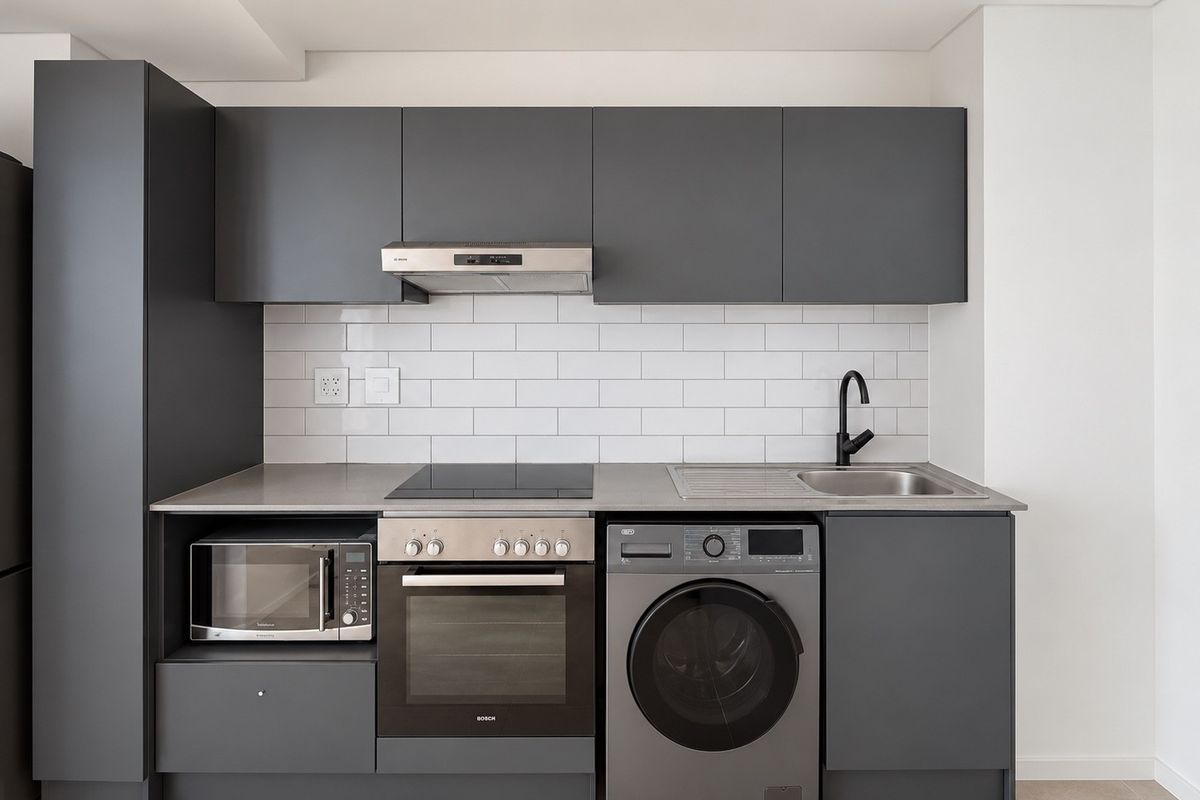 Modern kitchen featuring charcoal cabinetry, subway tile backsplash, integrated appliances including an oven, hob, extractor, microwave, and washing machine with a stainless steel sink.