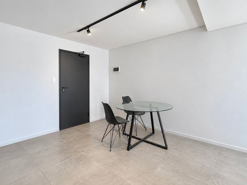 A minimalist living area featuring neutral tiled flooring, modern track lighting, and a sleek dark interior door.