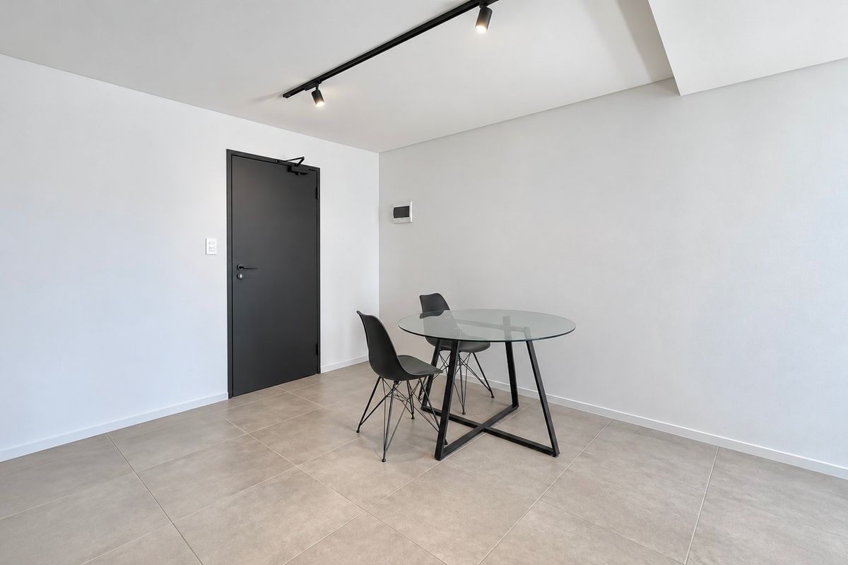 A minimalist living area featuring neutral tiled flooring, modern track lighting, and a sleek dark interior door.