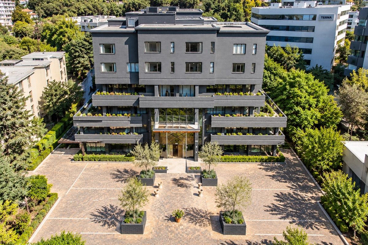 Aerial view of a modern multi-story apartment building featuring a paved entrance courtyard, landscaped planters, and private balconies on each level.