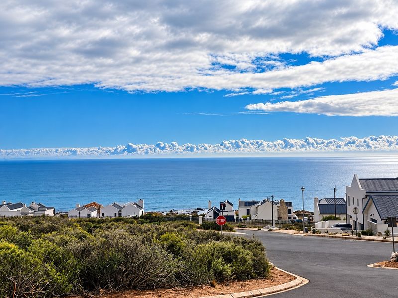 A scenic elevated view overlooking the coastline, ocean, and surrounding residential neighborhood with a clear paved road in the foreground.