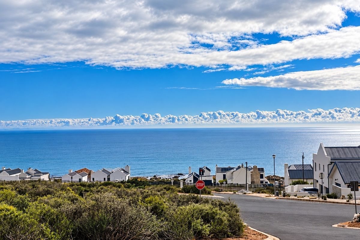 A scenic elevated view overlooking the coastline, ocean, and surrounding residential neighborhood with a clear paved road in the foreground.
