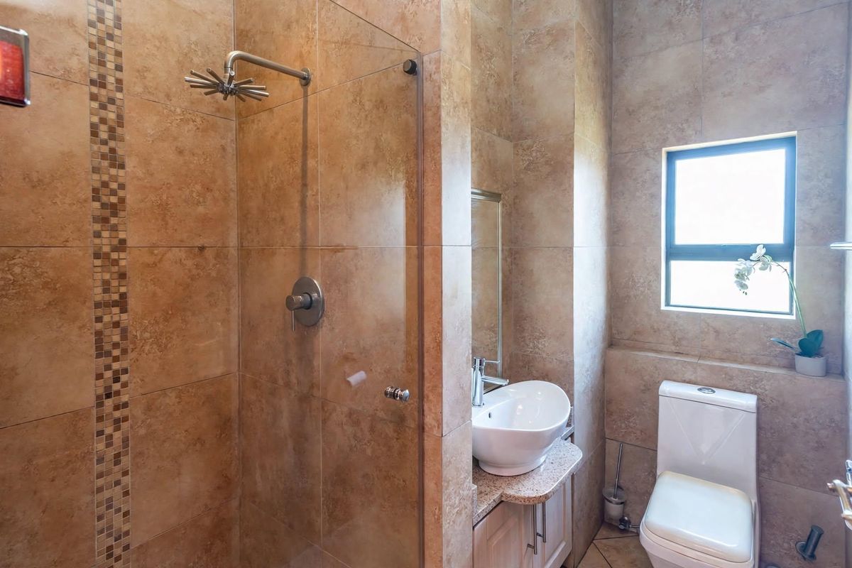 A modern bathroom featuring a walk-in shower with glass screen, vessel sink on a granite vanity, and neutral floor-to-ceiling tiling.