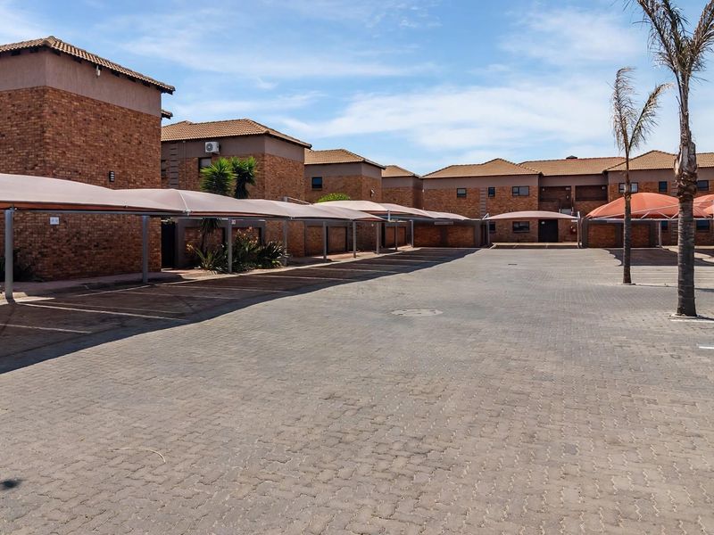 A well-maintained residential complex featuring a large paved parking area with covered carports and classic brick building facades.