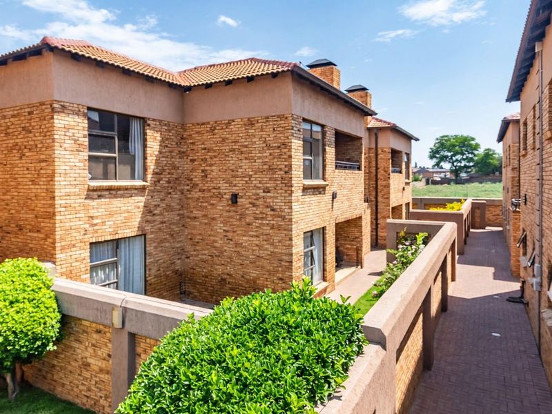 A view of the rear exterior of a multi-story face brick residential complex featuring paved walkways and established garden borders.