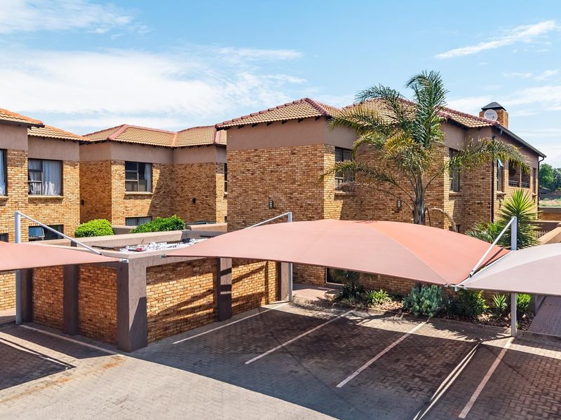 Exterior view of a face brick residential complex featuring a paved driveway with shade cloth carports and established landscaping.