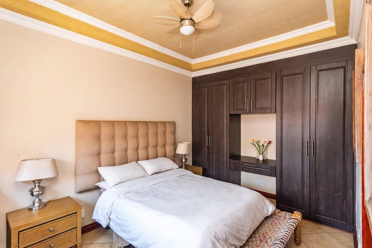 A well-maintained bedroom featuring built-in dark wood cabinetry, a ceiling fan, and crown molding, providing a functional and comfortable living space.