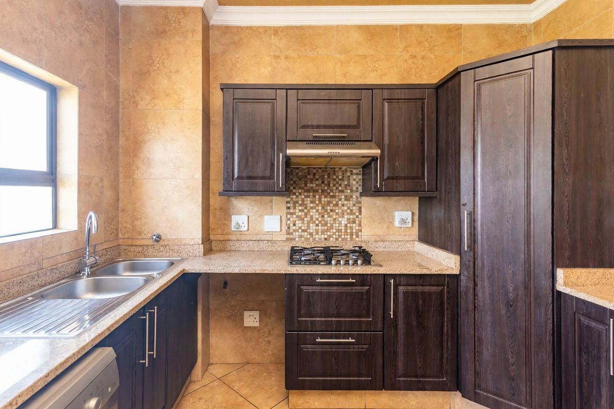 A functional kitchen featuring dark wood cabinetry, granite countertops, a gas hob with extractor fan, and a double sink with tiled finishes.