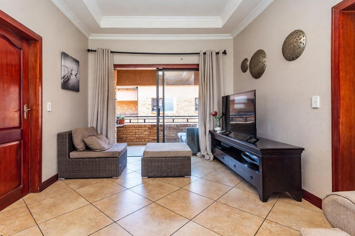 A well-maintained living room featuring ceramic tile flooring, a decorative tray ceiling, and a sliding glass door providing access to an outdoor balcony.