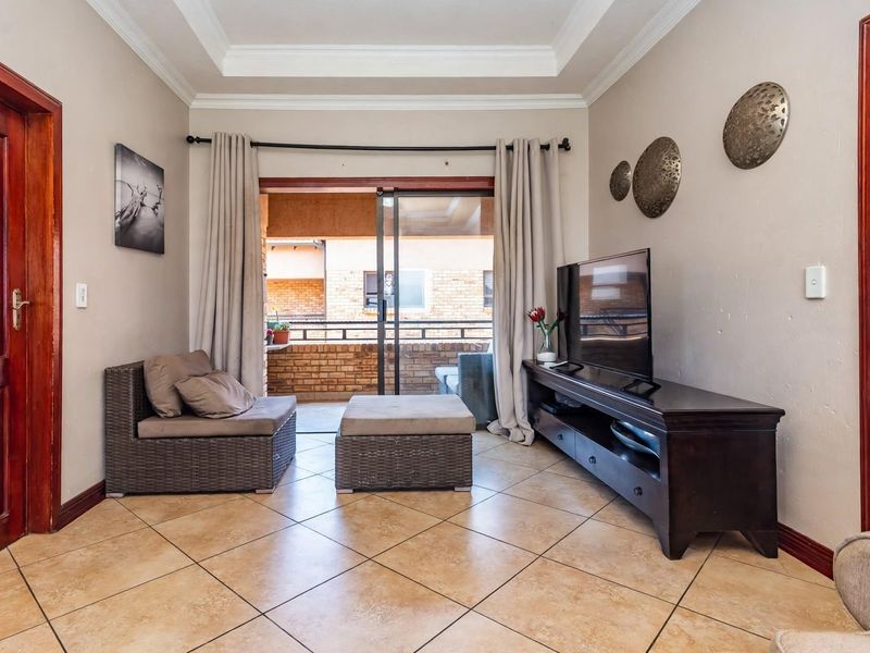 A well-maintained living room featuring ceramic tile flooring, a decorative tray ceiling, and a sliding glass door providing access to an outdoor balcony.