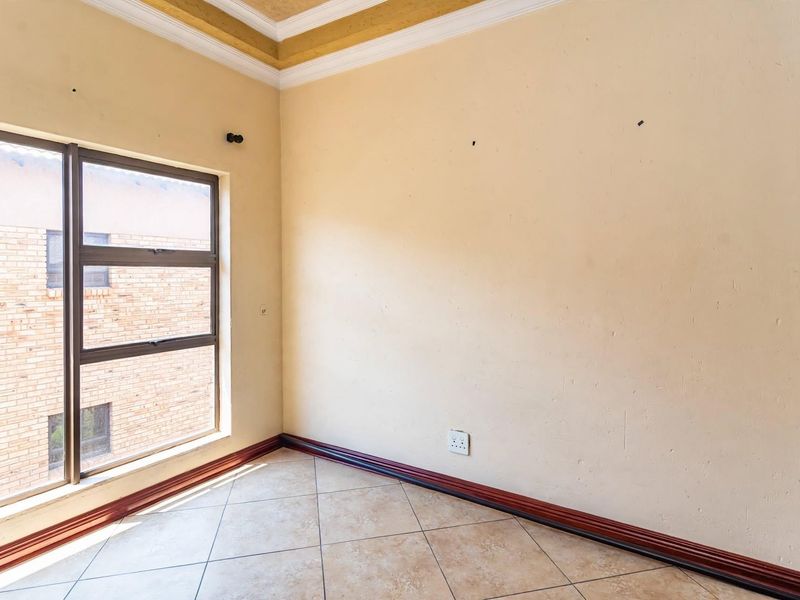 An empty bedroom featuring tiled flooring, built-in cupboards, and a large aluminium window providing natural light.