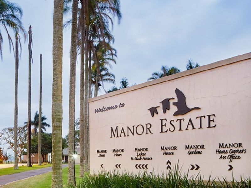 Entrance signage for Manor Estate featuring directional markers and landscaped surroundings.