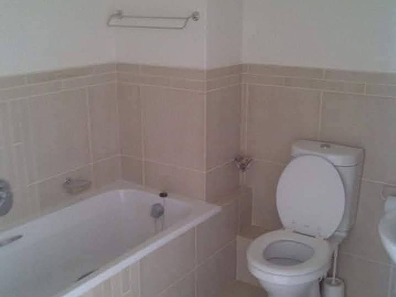 A functional bathroom featuring a bathtub, toilet, and neutral ceramic wall tiling throughout.