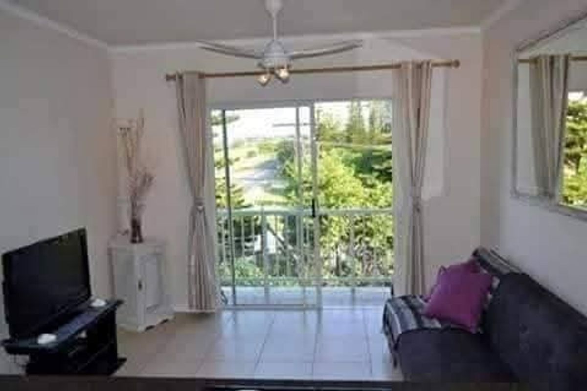 A living room featuring tiled flooring, a ceiling fan, and a sliding glass door that opens onto a balcony with outdoor views.