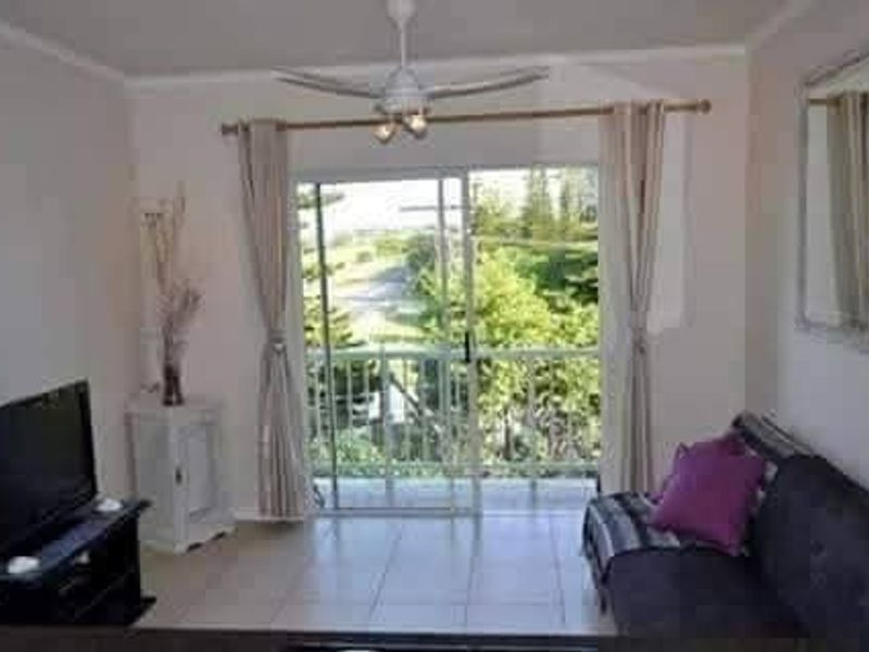 A living room featuring tiled flooring, a ceiling fan, and a sliding glass door that opens onto a balcony with outdoor views.