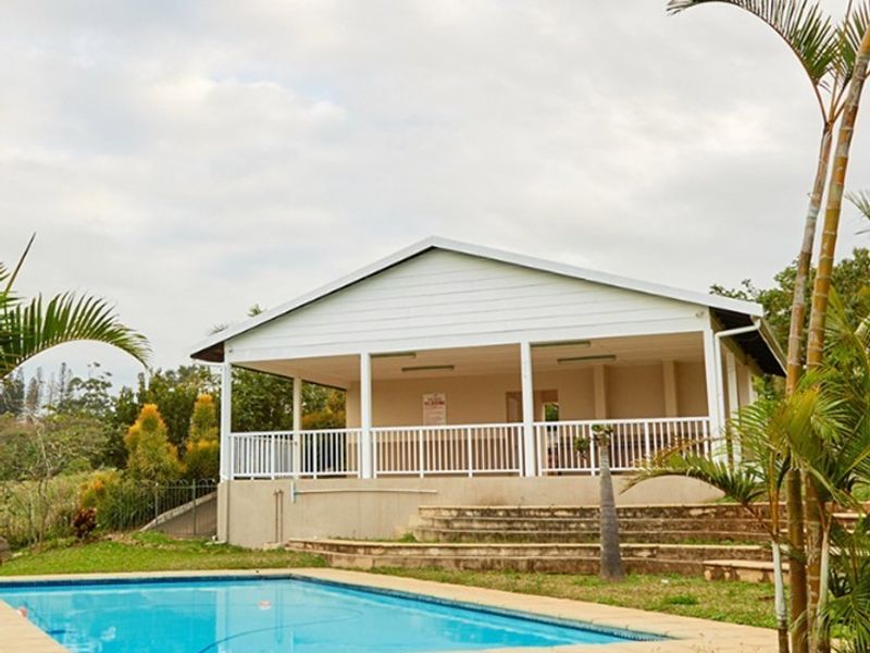 Outdoor pool area featuring a swimming pool and a covered patio structure with white railings, set within a landscaped garden.