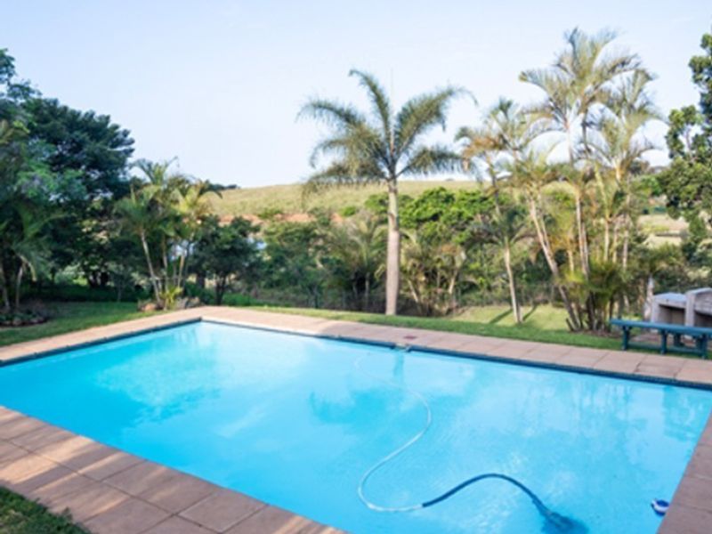 A well-maintained outdoor swimming pool area featuring a tiled surround, built-in braai, and scenic garden views.