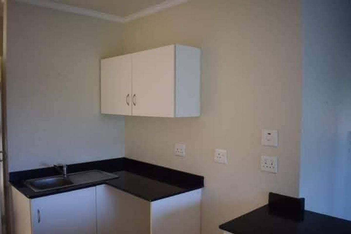 A compact kitchen area featuring white built-in cabinetry, dark laminate countertops, and a stainless steel sink with a mixer tap.