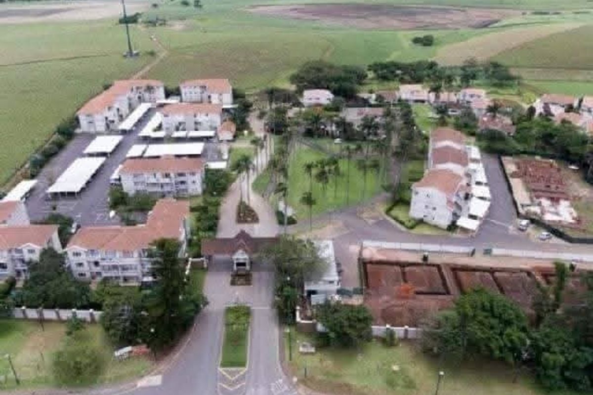 Aerial view of a residential apartment complex featuring multiple buildings, covered parking areas, landscaped grounds, and a secure gated entrance.