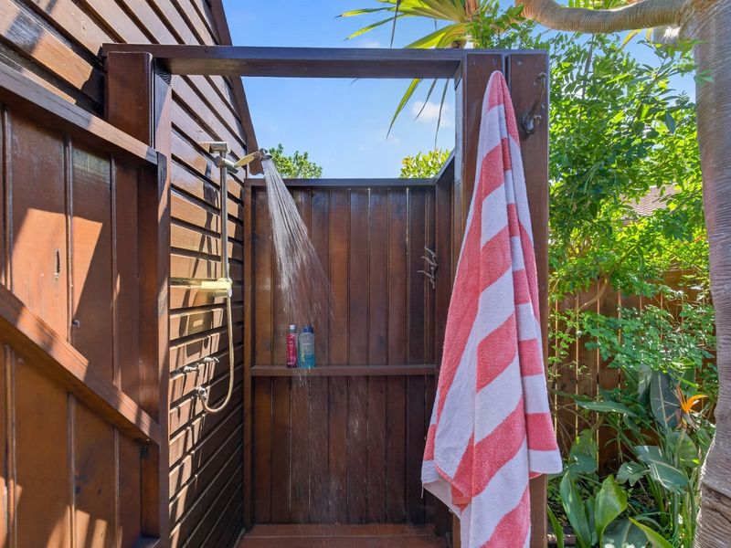 An outdoor shower area featuring timber cladding and decking, providing a convenient wash-up space in a garden setting.