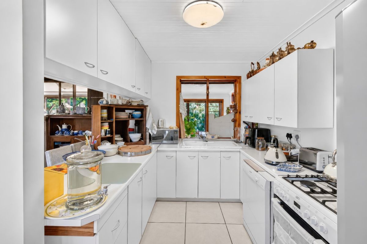 A functional kitchen featuring white cabinetry, tiled flooring, a gas hob, and a double sink with a view through to the adjacent living area.