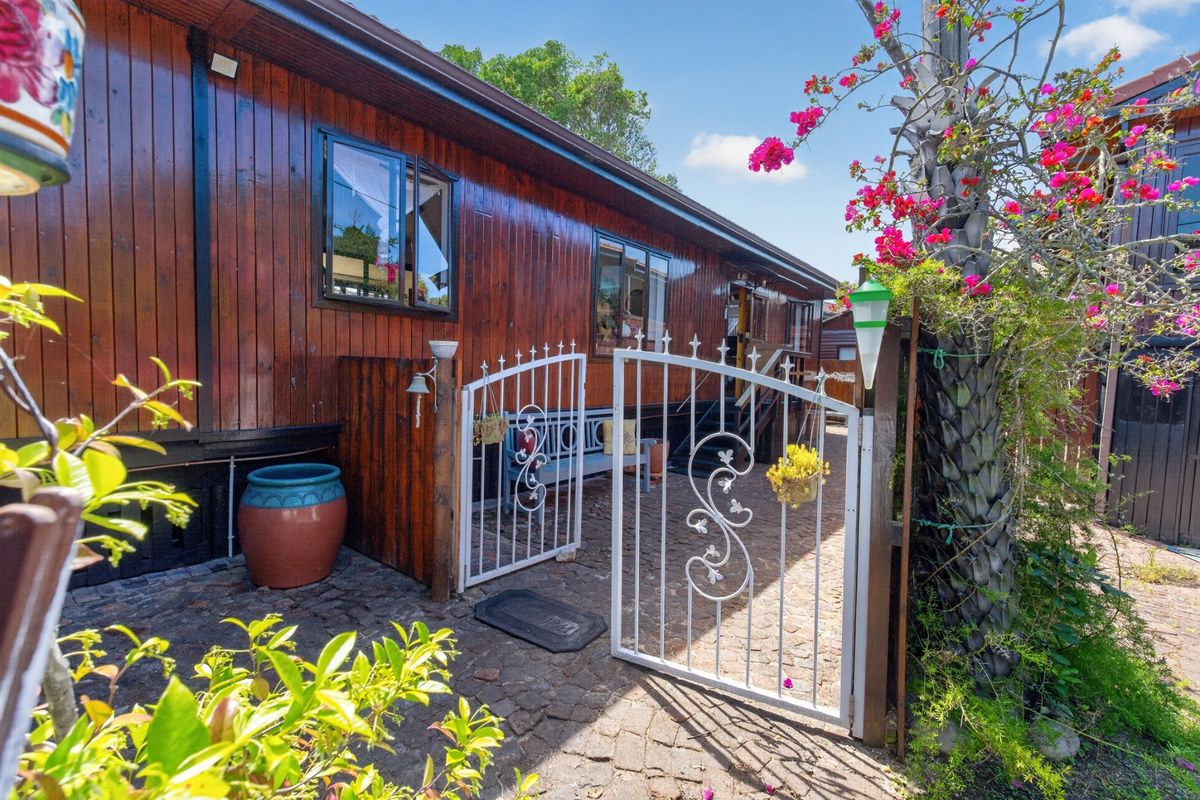 A rear exterior view featuring timber-clad walls, a decorative wrought iron gate, and cobblestone paving in a garden setting.