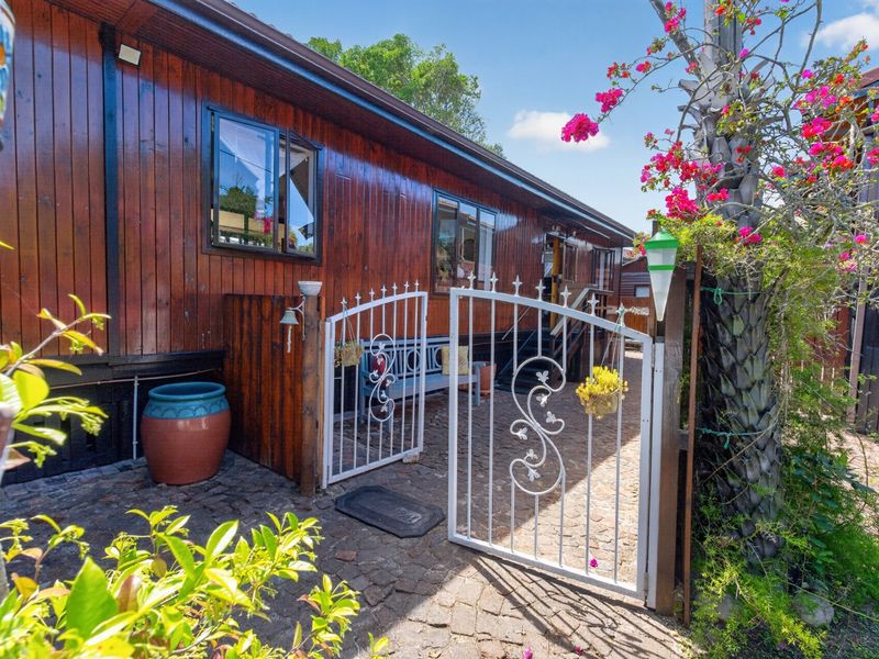 A rear exterior view featuring timber-clad walls, a decorative wrought iron gate, and cobblestone paving in a garden setting.