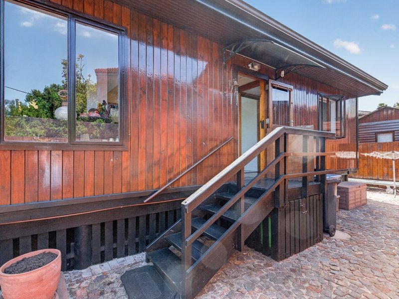 Rear exterior view of a timber-clad house featuring a staircase with railings and cobblestone paving.