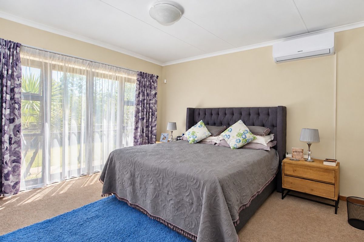 A well-lit bedroom featuring carpet flooring, a split-system air conditioner, and large sliding glass doors that provide natural light and garden access.
