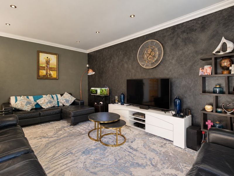 A well-maintained living room featuring a dark textured accent wall, recessed downlighting, and decorative crown molding, creating a sophisticated and modern atmosphere.
