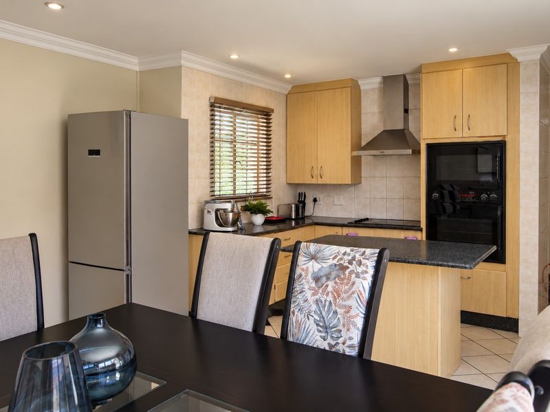 Open-plan kitchen featuring light wood cabinetry, granite countertops, and integrated stainless steel appliances, seamlessly flowing into the dining area with tiled flooring.