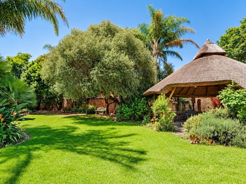 A well-maintained garden featuring a traditional thatched gazebo, lush green lawn, and mature trees, providing a serene outdoor space.