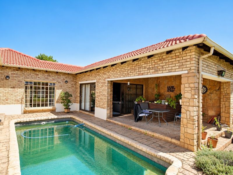 Outdoor pool area featuring a covered patio with stone-clad pillars, brick exterior walls, and a paved deck, perfect for relaxation and entertaining.